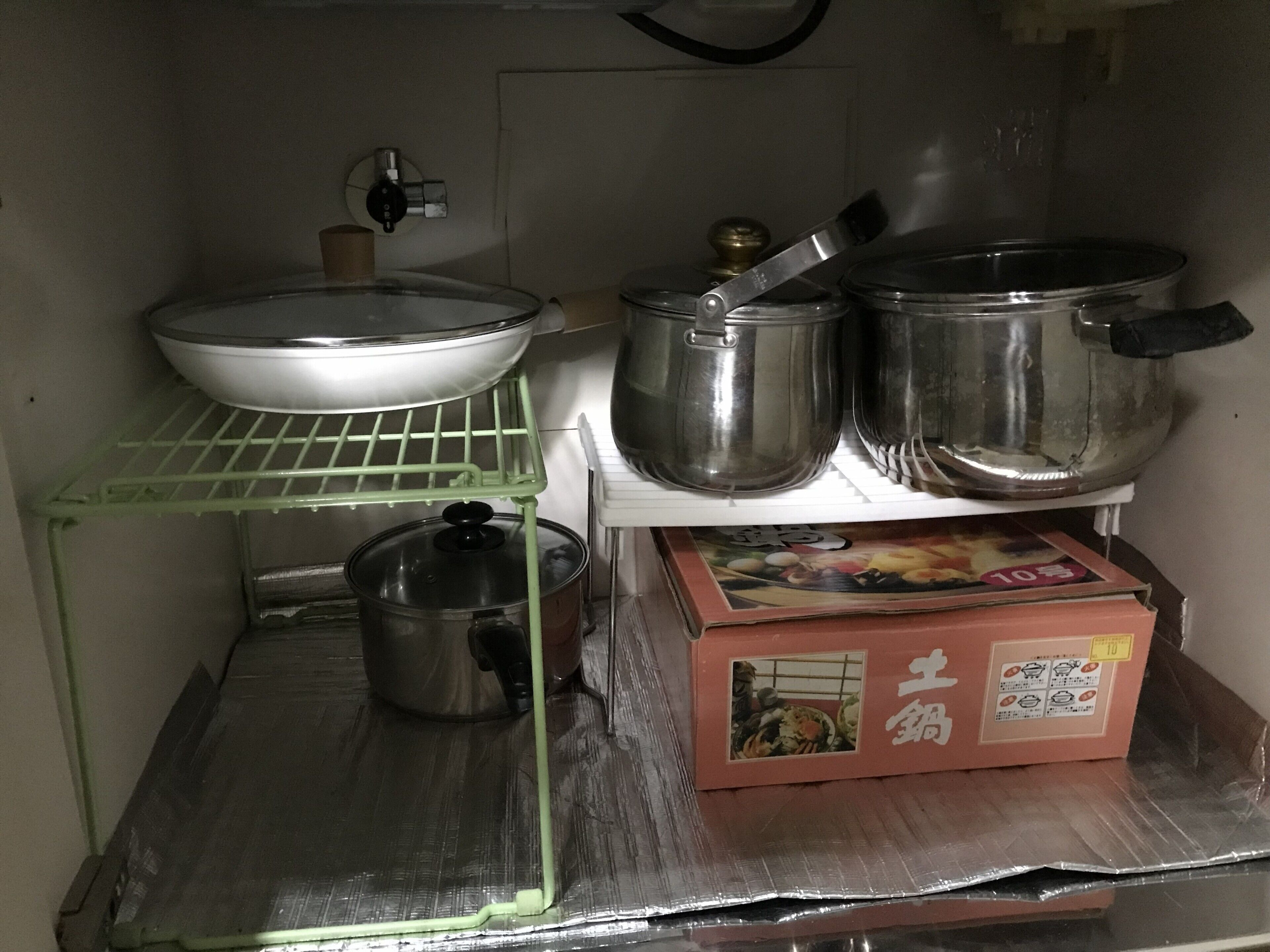 A kitchen with stainless steel cookware, a green shelf, and a box with Asian characters.