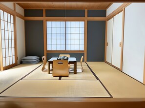 Una habitación con tatamis, una mesa baja, sillas y una ventana con puertas correderas.