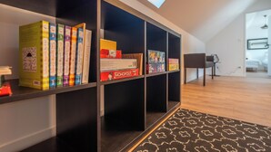 Ein modernes Interieur mit einem Bücherregal voller Gegenstände, einem gemusterten Teppich und Blick auf einen Raum mit einem Sessel und einem Schreibtisch.