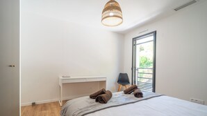 Ein Schlafzimmer mit einem Bett, einem Nachttisch, einem Sessel, einem Fenster und einer Pendelleuchte.
