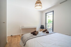 A bedroom with a bed, a bedside table, a chair, a window, and a hanging light fixture. - Villa Les Patys (Vouvray)