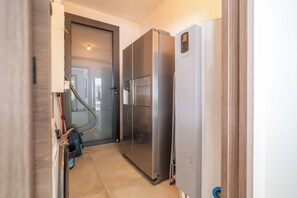 A narrow hallway with a vacuum cleaner, a refrigerator, and a door leading to another room. - Villa Les Patys (Vouvray)
