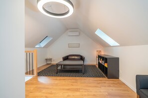 A modern loft bedroom with a skylight, a leather sofa, a small table, and a bookshelf. - Villa Les Patys (Vouvray)