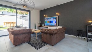 Ein modernes Wohnzimmer mit einem großen Flachbildfernseher an einer dunklen Wand, zwei braunen Ledersofas, einem Holztisch und einem gemusterten Teppich.