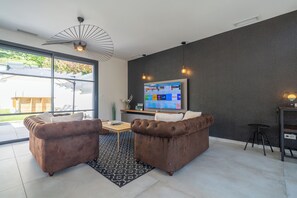 A modern living room with a large flat-screen TV mounted on a dark wall, two brown leather sofas, a wooden coffee table, and a patterned rug. - Villa Les Patys (Vouvray)