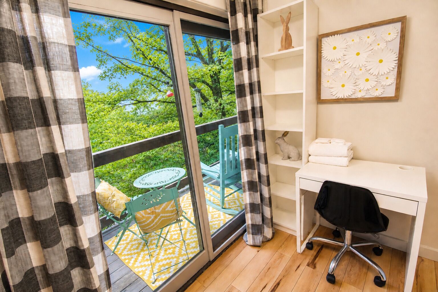A balcony with a table and chairs, a white desk with a chair, and a shelf with decorative items.