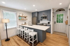 Une cuisine moderne dotée d’un îlot central, de tabourets de bar, d’un réfrigérateur, d’un four à micro-ondes et d’une cuisinière.