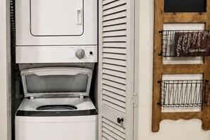 A compact, white laundry room with a built-in washer and dryer, a wooden door with a metal rack, and a small shelf with a sign. - Beech Mountain Getaway with Fireplace & Views (Beech Mountain)