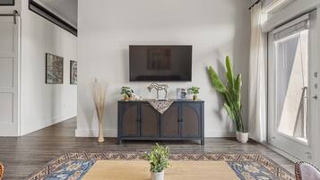 Un salon moderne avec un meuble en bois foncé, un téléviseur à écran plat fixé au mur, une grande plante en pot et un tapis à motifs.
