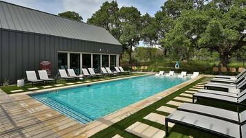 A swimming pool with lounge chairs, a building with large windows, and a grassy area.