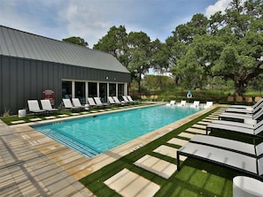 A swimming pool with lounge chairs, a building with large windows, and a grassy area.