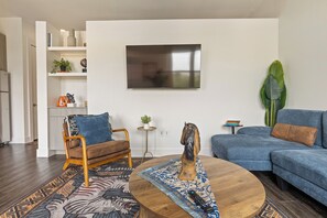 A modern living room with a sofa, armchair, coffee table, and a television mounted on the wall. - 1BR Retreat Near Pool, Gym & Clubhouse SHI 2405 (Austin)