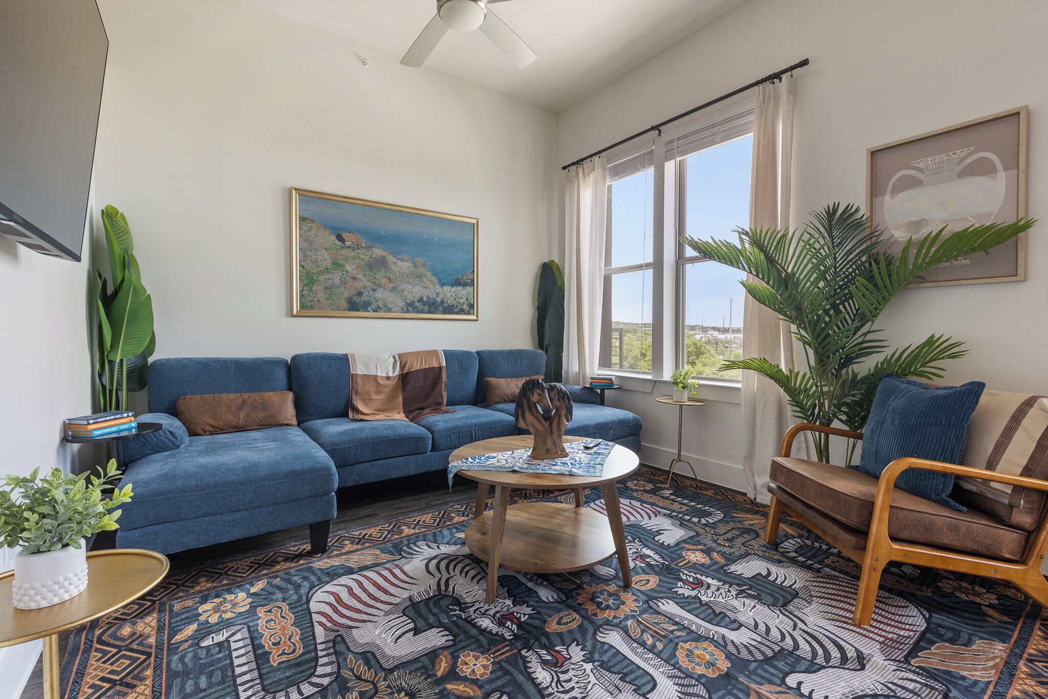 Una sala de estar con un sofá azul, una mesa de centro redonda y vistas al exterior a través de grandes ventanales.