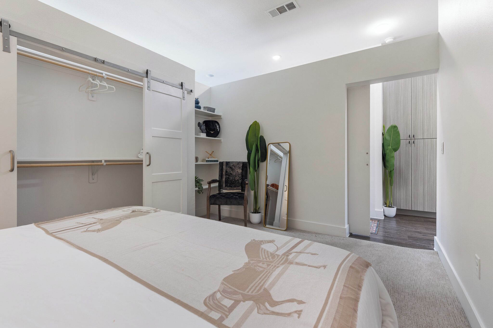 Un dormitorio con cama, armario, espejo, una silla y una planta en maceta.