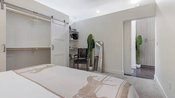 Un dormitorio con cama, armario, espejo, una silla y una planta en maceta.