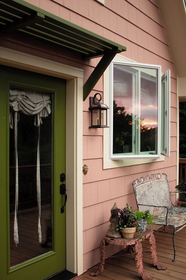 A house with a green door, a white window, and a porch with a chair and a table.