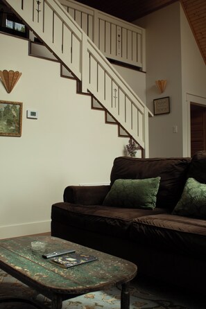 A living room with a brown sofa, a wooden coffee table, a staircase, and a framed picture on the wall.