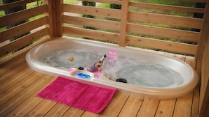 A hot tub with a pink towel, a bottle, and a glass on the deck.