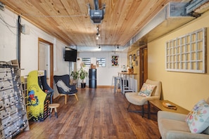 A room with wooden flooring, a sofa, a chair, a foosball table, and a television.