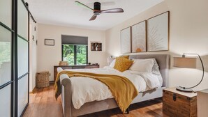 A bedroom with a bed, bedside table, lamp, window, and artwork on the wall.