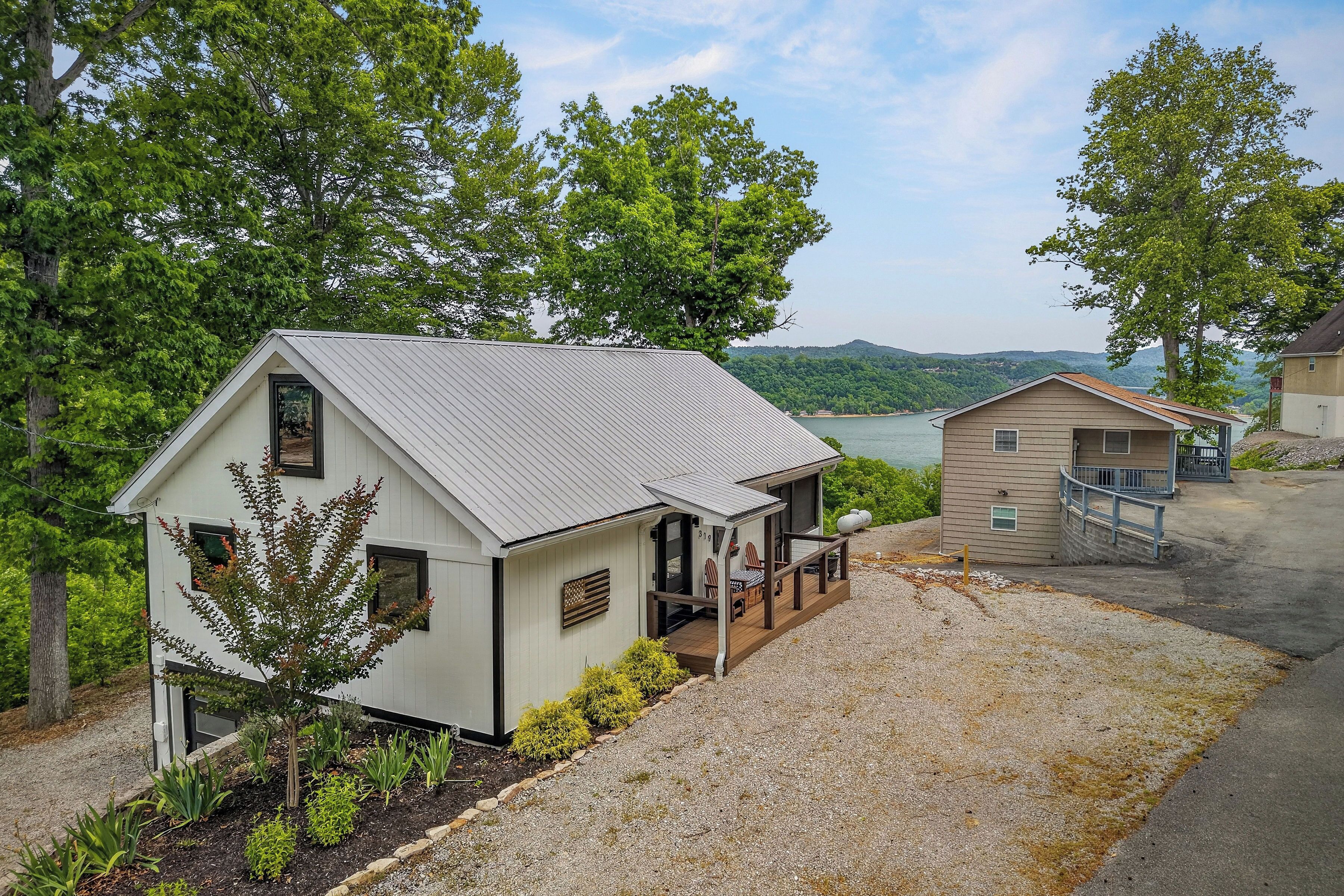 A small cabin with a porch, a deck, and a view of a lake and mountains.