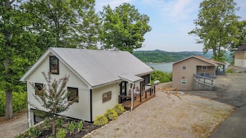 A small cabin with a porch, a deck, and a view of a lake and mountains.