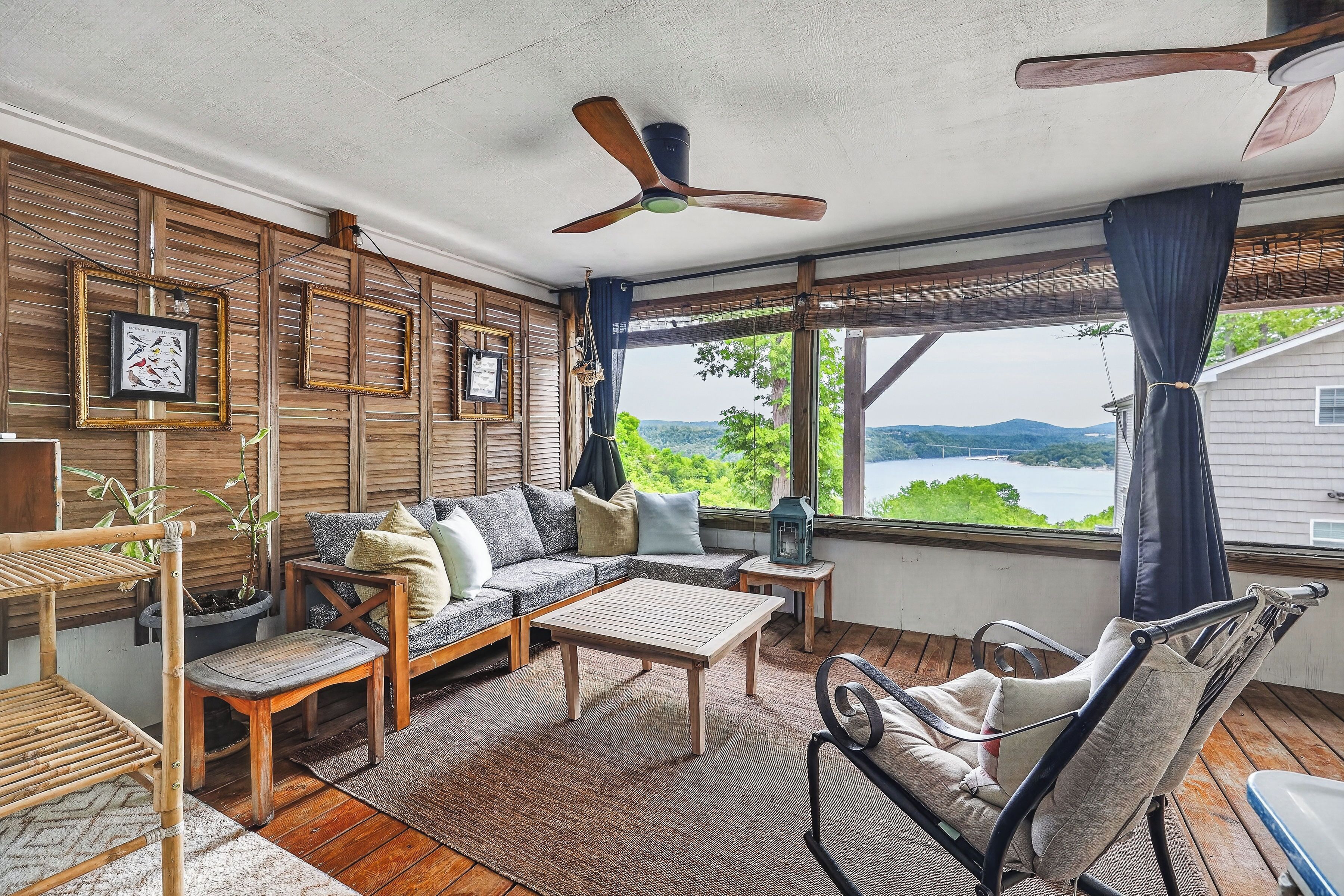 A cozy room with a wooden ceiling fan, a sofa, a table, and a view of a lake.