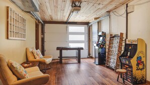 A room with wooden flooring, a pool table, two leather chairs, a foosball table, and a Pac-Man arcade machine.