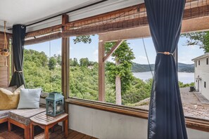 Ein Zimmer mit großem Fenster mit Blick auf einen See und einen Wald, eine hölzerne Bank und eine hängende Leuchte.