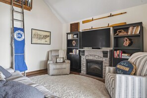 A living room with a fireplace, bookshelves, a television, and a ladder against the wall.