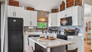A modern kitchen with white cabinetry, a black refrigerator, a wooden island with bar stools, and a patterned backsplash.
