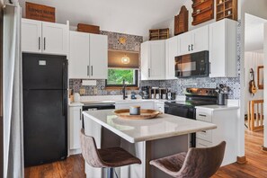 A modern kitchen with white cabinetry, a black refrigerator, a wooden island with bar stools, and a patterned backsplash.