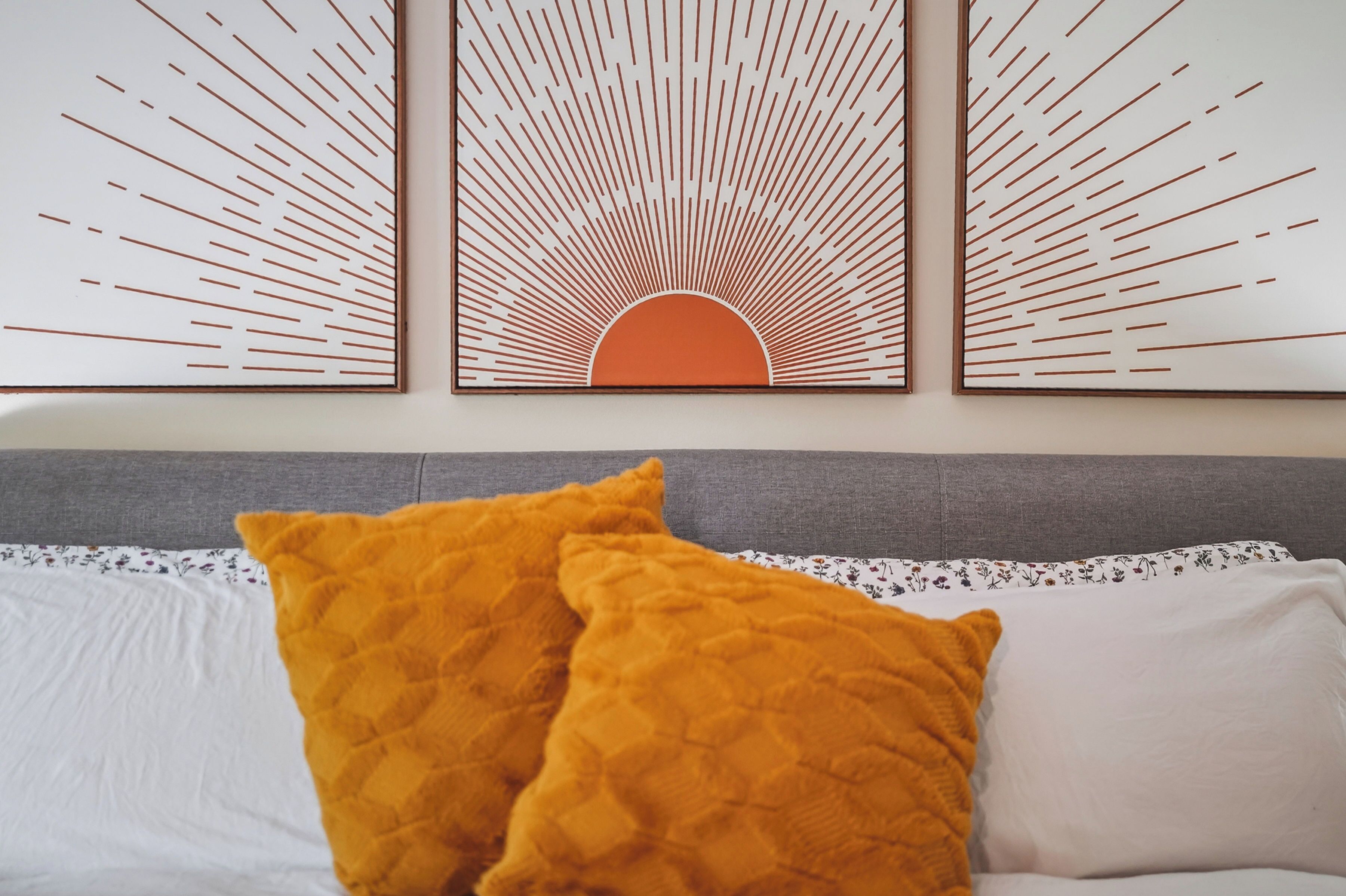 A bed with two pillows, a grey headboard, and a wall with three framed artworks.