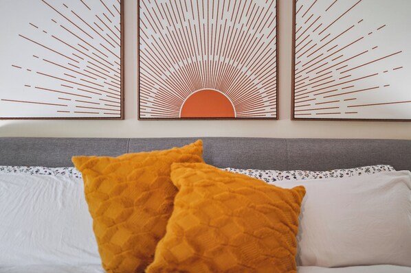 A bed with two pillows, a grey headboard, and a wall with three framed artworks.