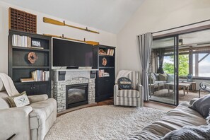 A cozy living room with a fireplace, bookshelves, a television, and a view of the outdoors. - View of Sunset Marina and Dale Hollow Lake (Byrdstown)