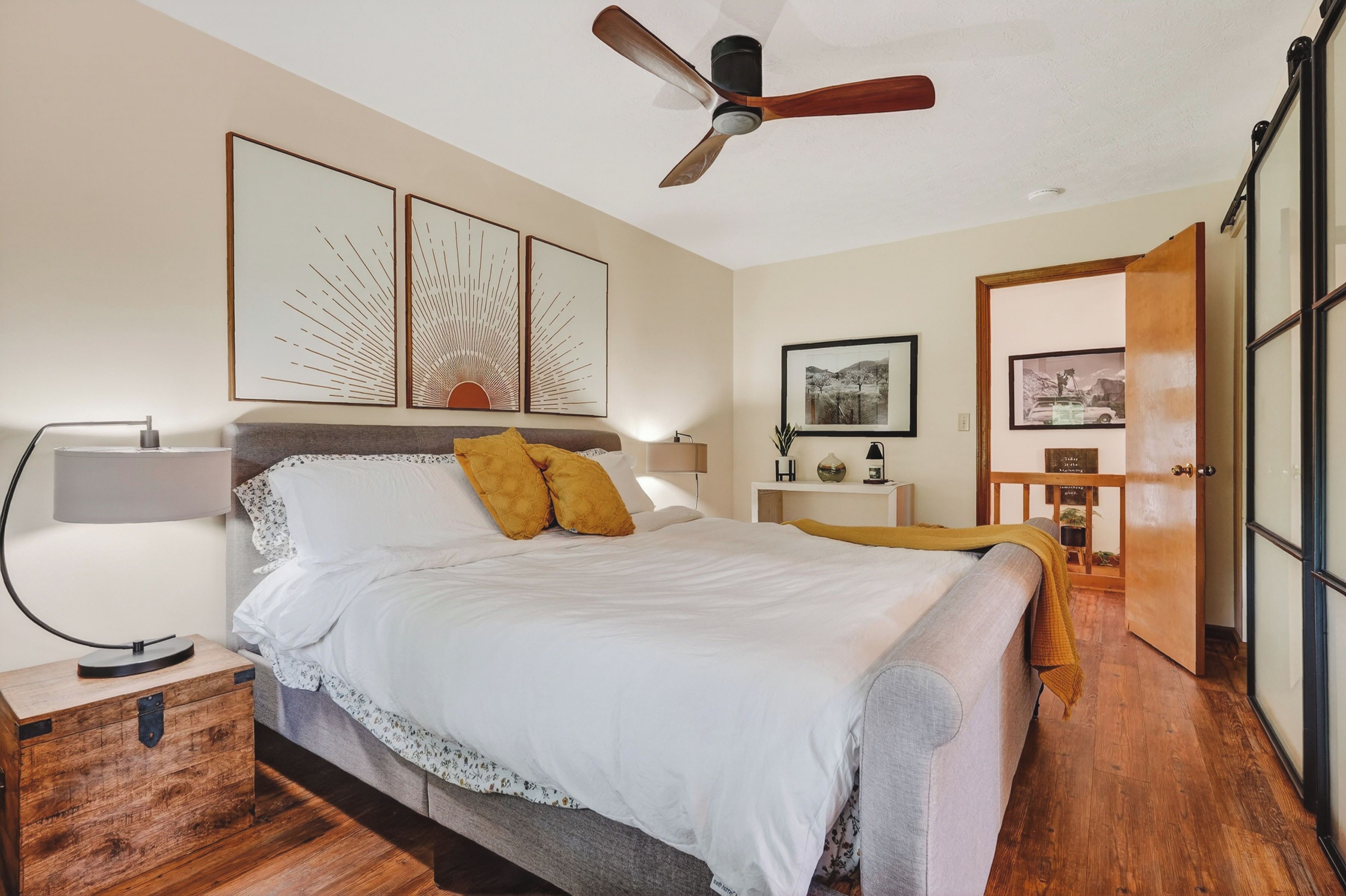 A bedroom with a bed, a nightstand, a bedside lamp, a ceiling fan, and artwork on the wall.