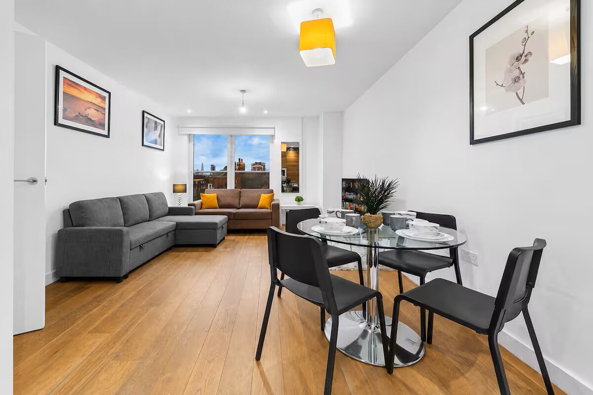 A modern living room with a sectional sofa, a dining table with chairs, and a large window offering a view of the cityscape.