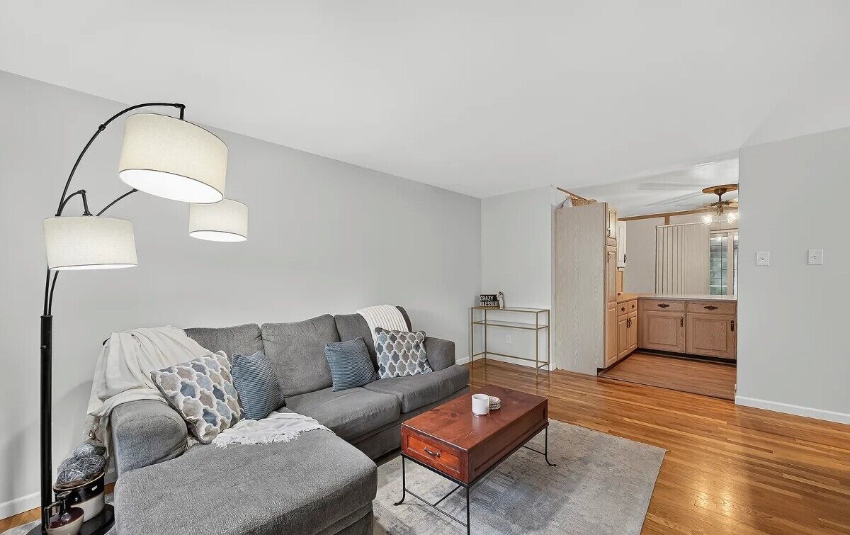 Ein modernes Wohnzimmer mit einem grauen Sofa, einem Holztisch und einer Stehlampe.