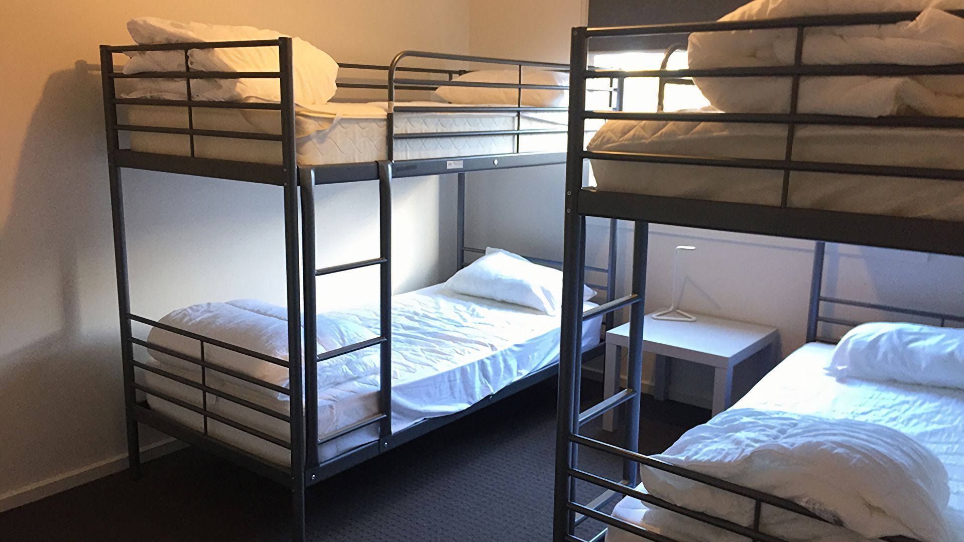 Une chambre avec trois lits superposés, chacun étant équipé de draps blancs. Une petite table de chevet avec une lampe se trouve sur le côté droit.