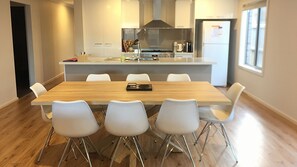 A modern kitchen with a central island, white chairs, and a wooden dining table. - Lakeside - Point Lonsdale (POINT LONSDALE)