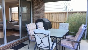Eine Außenpatio mit Glastür zu einem Wohnzimmer, ein Grill und ein Tisch mit Stühlen.