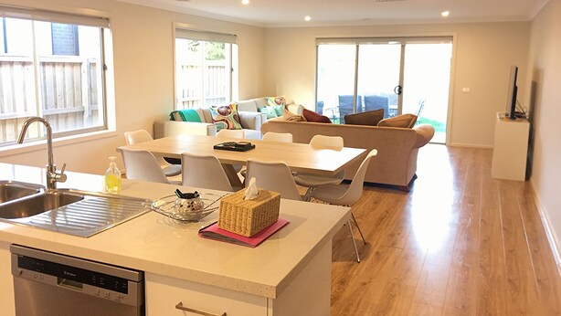 Eine moderne Küche mit Geschirrspüler, ein Essbereich mit Tisch und Stühlen sowie ein Wohnbereich mit Sofa und Kissen.
