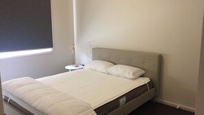 Ein ordentlich bezogenes Bett mit grauem Kopfteil und weißer Bettwäsche in einem Zimmer mit einem kleinen Nachttisch und einer Lampe.
