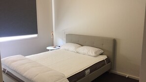 Ein ordentlich bezogenes Bett mit grauem Kopfteil und weißer Bettwäsche in einem Zimmer mit einem kleinen Nachttisch und einer Lampe.