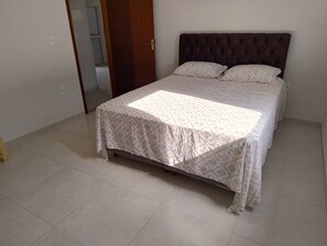 Una cama con colcha estampada, cabecero de madera y suelo de baldosas.
