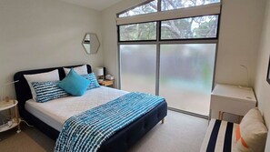 Ein Schlafzimmer mit einem Bett, Nachttisch, Lampe und einem großen Fenster.