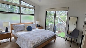 Ein Schlafzimmer mit einem Bett, zwei Nachttischen, einem Sessel, einem Kleiderschrank und einer Glastür zum Balkon.