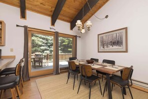 Un comedor con una mesa y sillas de madera, una araña y un cuadro en la pared.