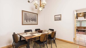 Uma sala de jantar com mesa de madeira, cadeiras pretas, um lustre e quadros nas paredes.
