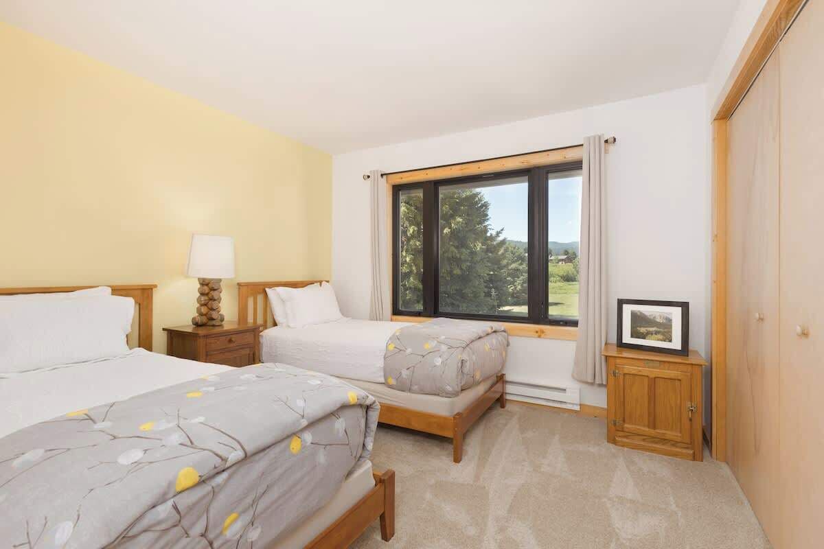 Een slaapkamer met twee bedden, een raam met uitzicht, een nachtkastje met lamp en een klein kastje.